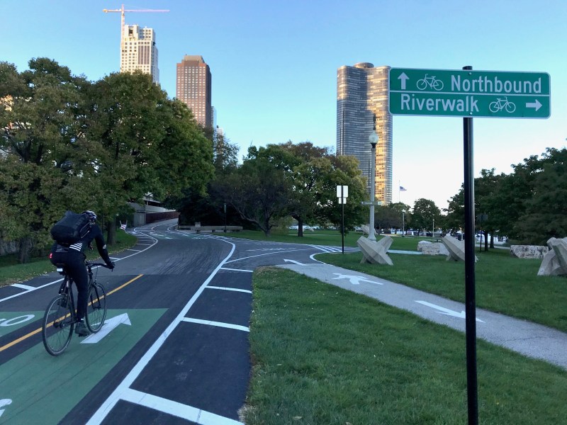 Signs and markings on the offramp from the Lakefront Trail to the riverwalk encourage people to bike to the promenade, but other signs threaten prosecution if they ride there. Photo: John Greenfield