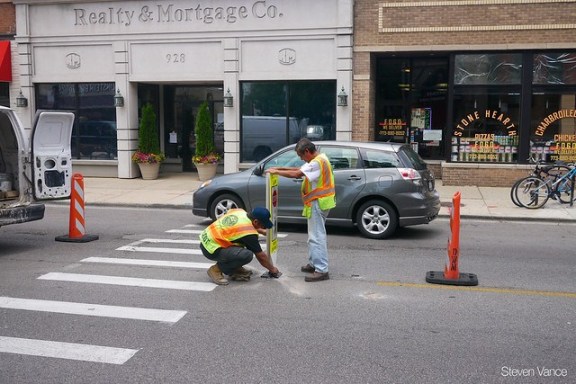 Workers install a "Stop for Pedestrians" sign. Photo: Steven Vance