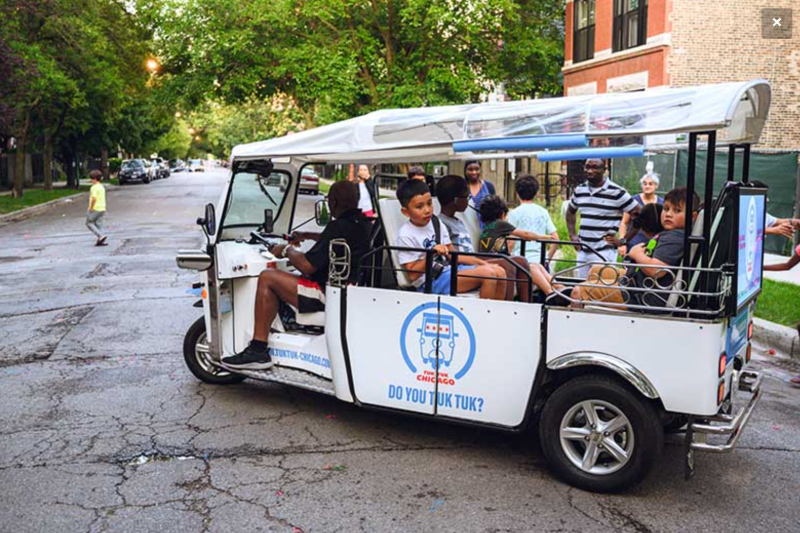 Kids take a Chicago Tuk Tuk ride at a community event.